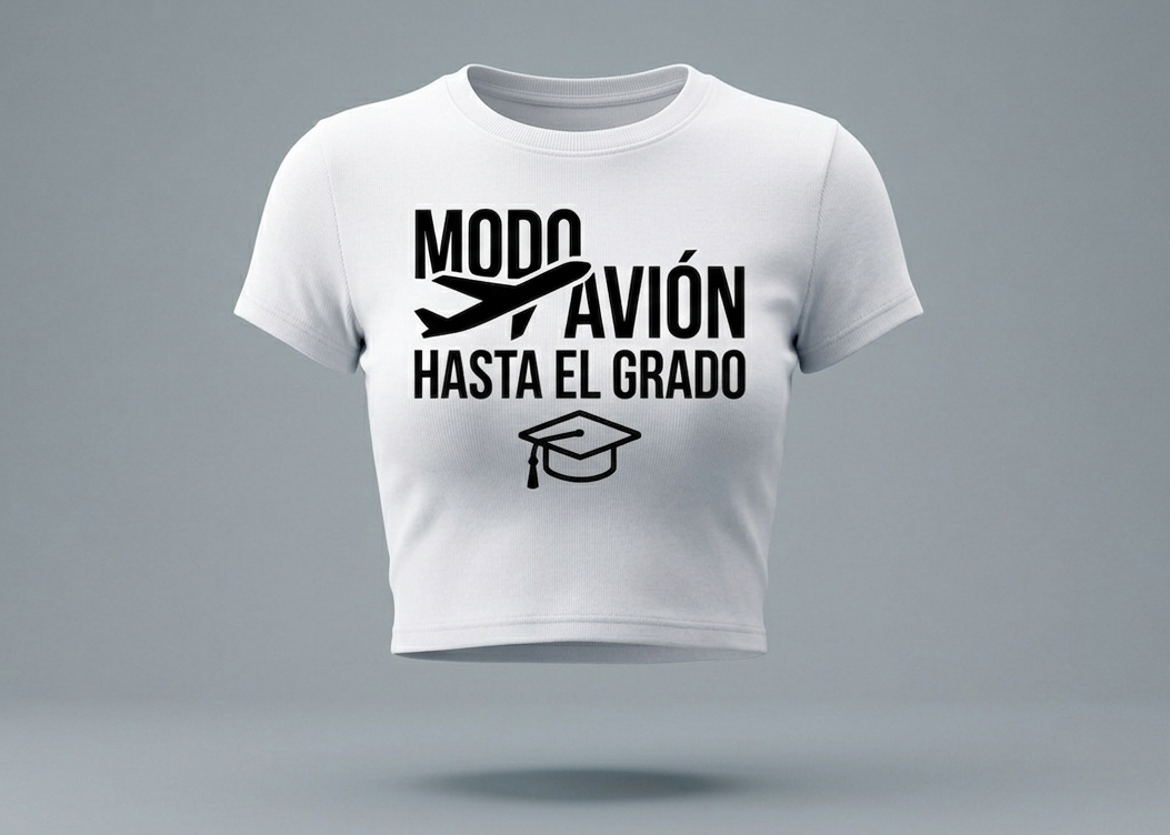 Mockup de un crop top blanco de cuello redondo con un diseño gráfico minimalista en color negro. El texto central dice "MODO AVIÓN HASTA EL GRADO" acompañado por el icono de un avión despegando y un birrete de graduación en la parte inferior. Fondo gris suave con iluminación de estudio.