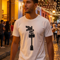 Joven vistiendo camiseta blanca con estampado de señalética urbana, caminando por una calle histórica iluminada con luces cálidas en el fondo, estilo lifestyle urbano.