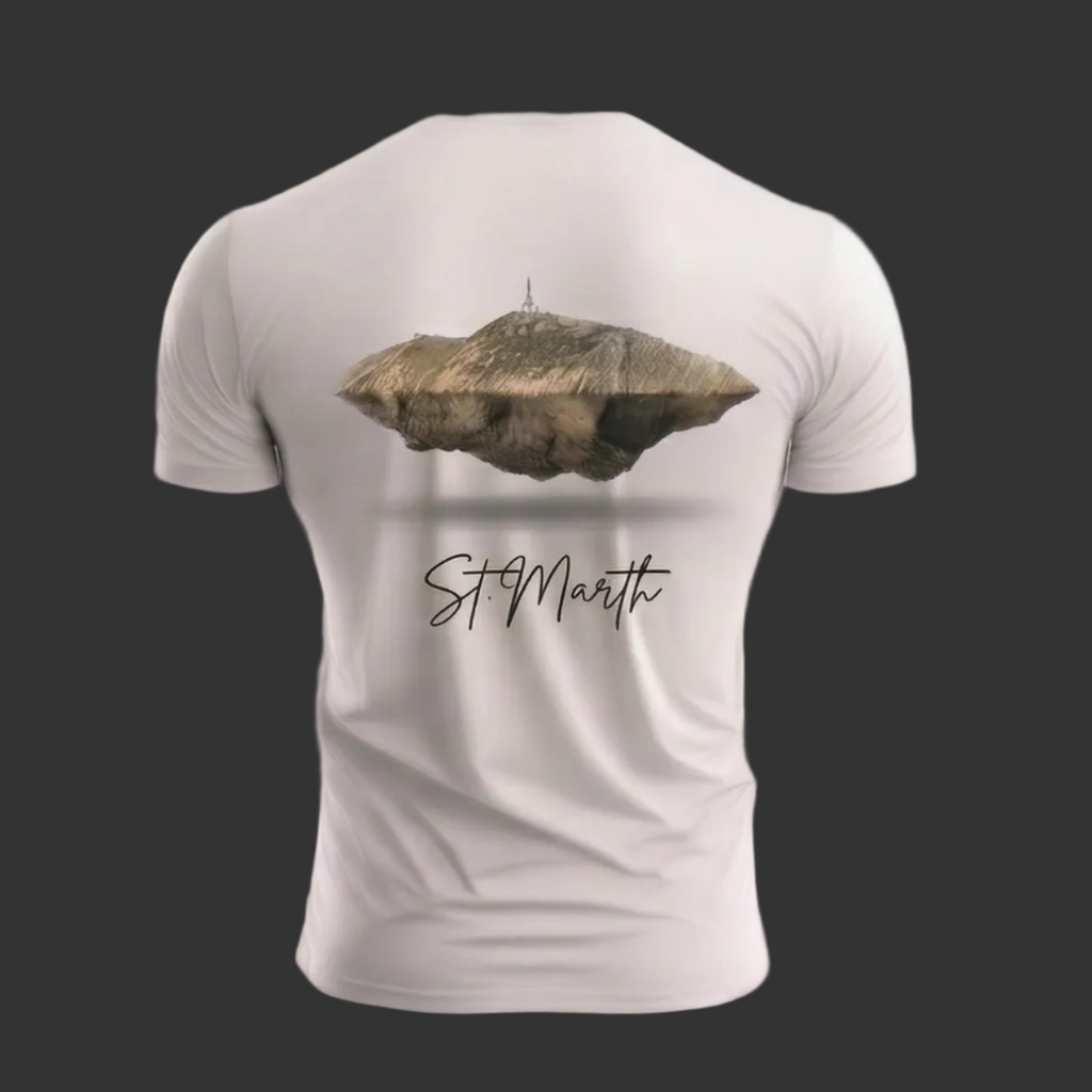Vista posterior de una camiseta blanca de hombre con un estampado detallado en la espalda que muestra una isla o montaña rocosa flotante con una estructura en la cima, seguida del texto en caligrafía negra 'St. Marth' sobre un fondo gris oscuro.