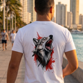 Hombre de espaldas caminando en un malecón urbano usando una camiseta blanca de trnd.ink con un estampado artístico de un lobo aullando en colores negro y rojo.