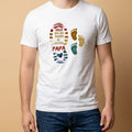 Mockup de un hombre vistiendo una camiseta blanca de manga corta con un diseño estampado para el Día del Padre de la marca Trnd.Ink. El gráfico central muestra la silueta de una huella de pie grande rellena con la frase "¡FELIZ DÍA DEL PADRE! AL MEJOR PAPÁ" en letras de colores, acompañada al lado por dos huellas pequeñas infantiles en tonos ocre y verde.