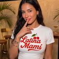 Camiseta blanca ajustada para mujer con el texto "Latina Mami" en letras rojas estilo retro y gráfico de cerezas, modelo posando en un ambiente lounge elegante.