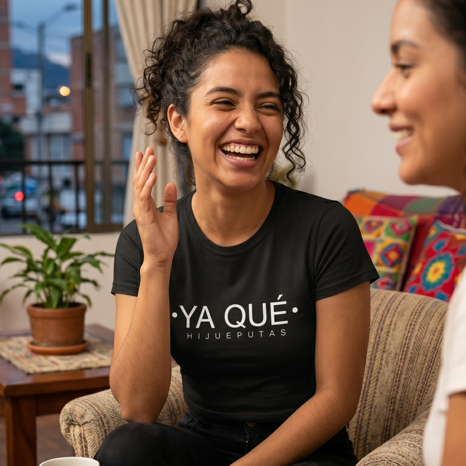 Mujer joven sonriendo usando una camiseta negra con la frase 'Ya Qué Hijueputas' en un ambiente casual, representando la moda urbana y cultura popular colombiana de trnd.ink.