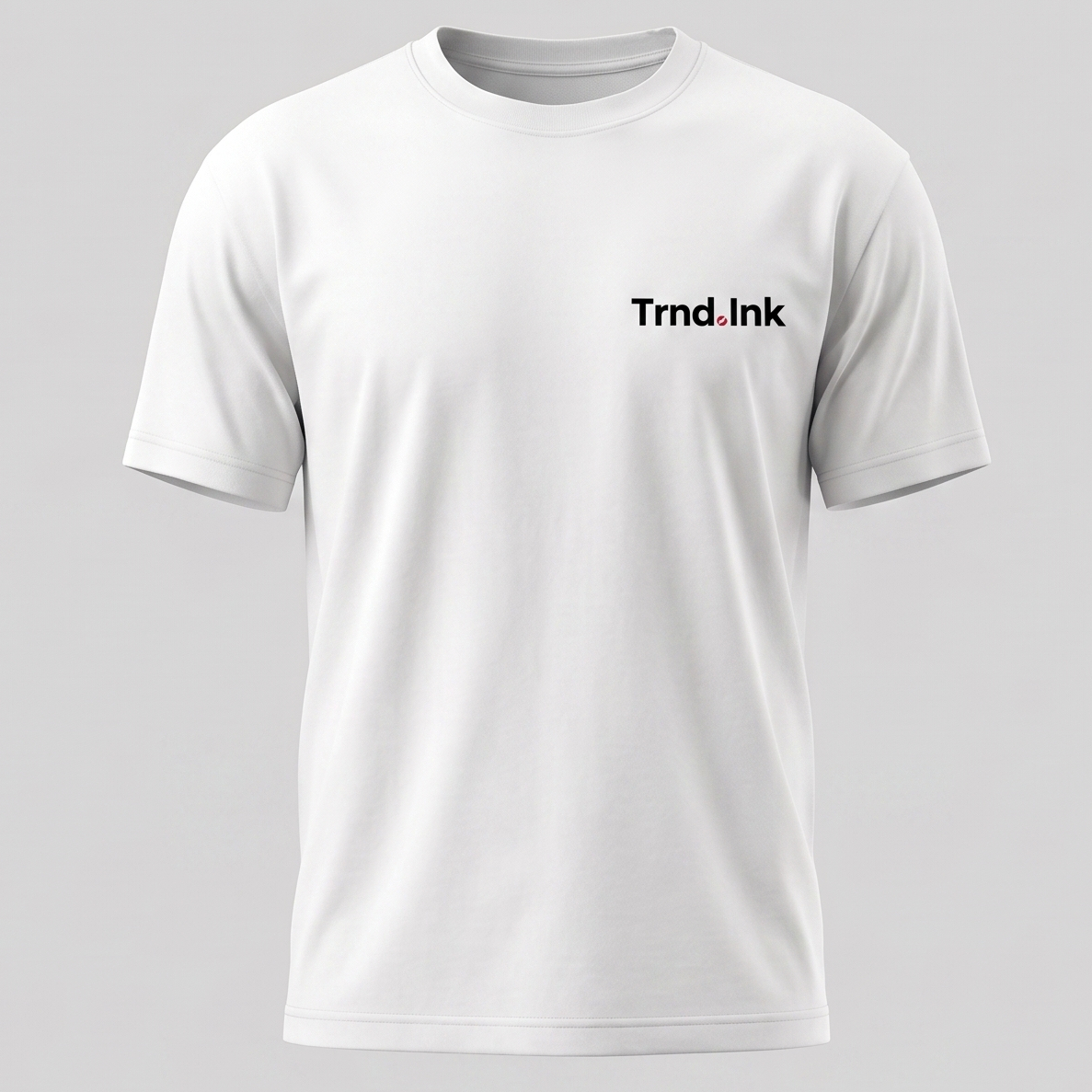 Una imagen de una camiseta blanca de manga corta y cuello redondo. La camiseta está colocada en un maniquí invisible y tiene un logotipo de "Trnd.Ink" impreso en el pecho izquierdo, en un pequeño rectángulo blanco con texto negro y un pequeño círculo rojo al final. El fondo es de color gris claro.