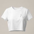 Una imagen de una camiseta corta blanca de cuello redondo y manga corta. La camiseta está colocada sobre un fondo gris claro y presenta un pequeño bordado negro en el pecho derecho que muestra dos colibríes de una línea volando uno hacia el otro. El bordado es delicado y minimalista.