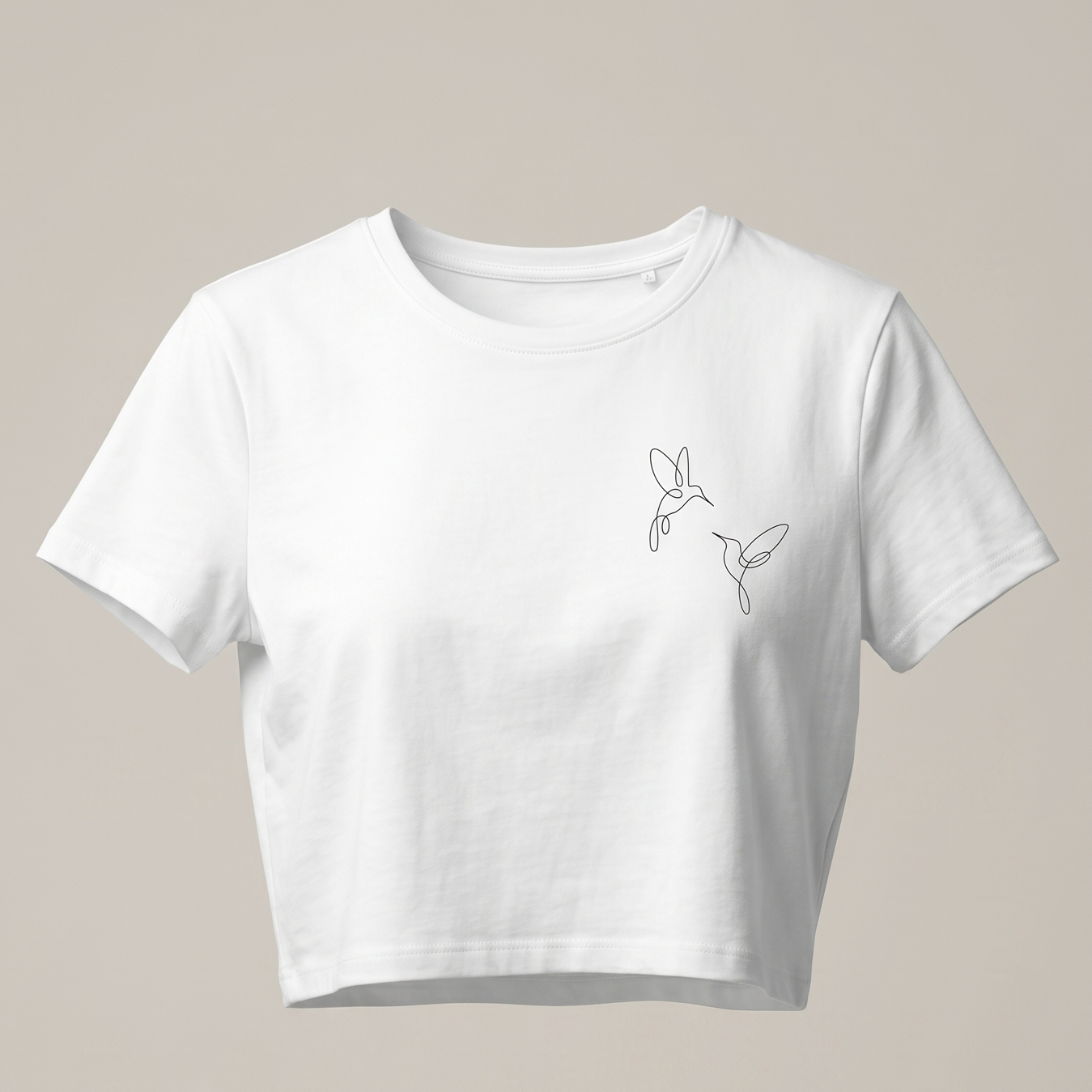 Una imagen de una camiseta corta blanca de cuello redondo y manga corta. La camiseta está colocada sobre un fondo gris claro y presenta un pequeño bordado negro en el pecho derecho que muestra dos colibríes de una línea volando uno hacia el otro. El bordado es delicado y minimalista.