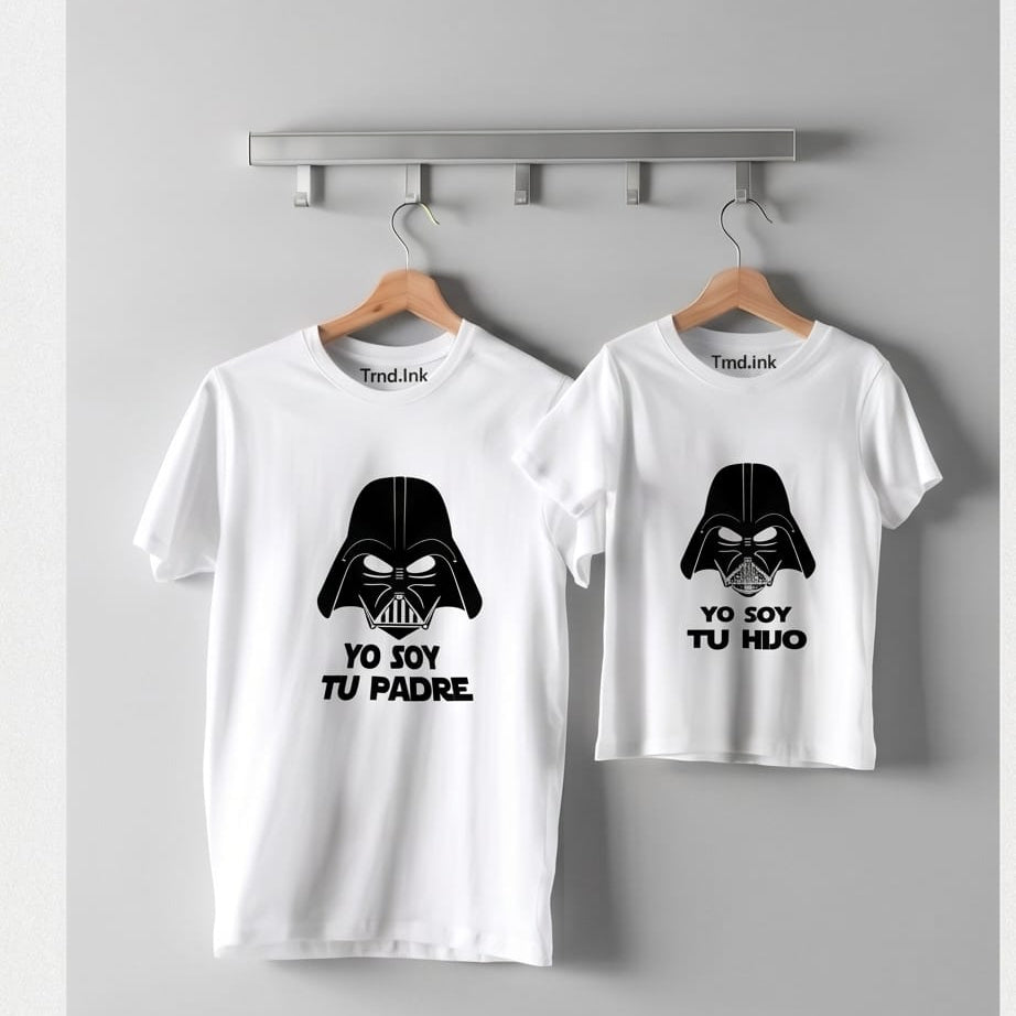 Fotografía de catálogo de dos camisetas blancas de manga corta (tamaño adulto e infantil) colgadas en ganchos de madera sobre un perchero metálico contra una pared gris neutra. Ambas prendas de la marca Trnd.Ink muestran un estampado central en tinta negra con el casco de Darth Vader; la camiseta de adulto lleva el texto "YO SOY TU PADRE" y la de niño "YO SOY TU HIJO". El logo de Trnd.Ink está ubicado de forma exacta en la parte superior central interna del cuello.