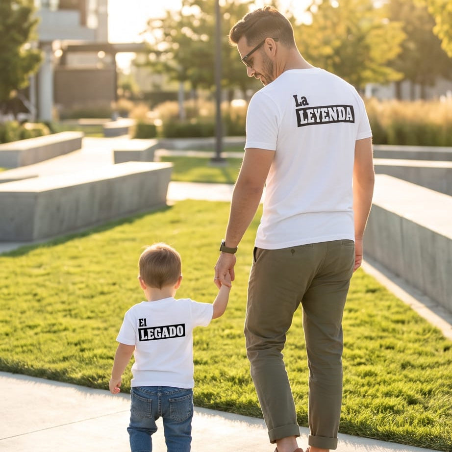 Un padre y su hijo pequeño caminan de espaldas de la mano usando camisetas blancas a juego de la marca Trnd.Ink. El estampado de la camiseta del padre dice "La Leyenda" y el del niño "El Legado", un diseño minimalista perfecto para regalo del Día del Padre.