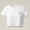 Camiseta tipo crop top de color blanco para mujer con diseño frontal minimalista. Presenta el texto 'QUE SE REPITA' en tipografía de máquina de escribir junto a un icono de flecha circular de repetición, todo enmarcado en un recuadro negro sobre un fondo gris neutro.