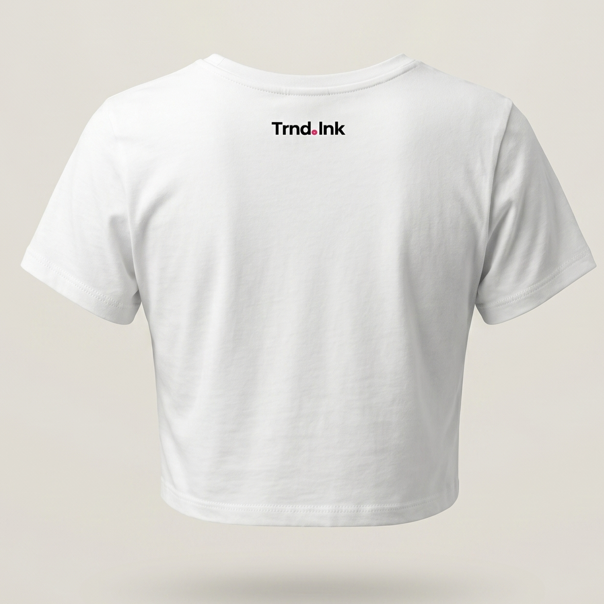 Vista trasera de crop top blanco para mujer con el logo de Trnd.Ink centrado bajo el cuello, fondo minimalista de estudio en tono hueso.