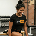 Mujer entrenando pierna en el gimnasio usando el crop top negro Gym Hub de Trnd.ink, realizando split squat sobre banco de madera.