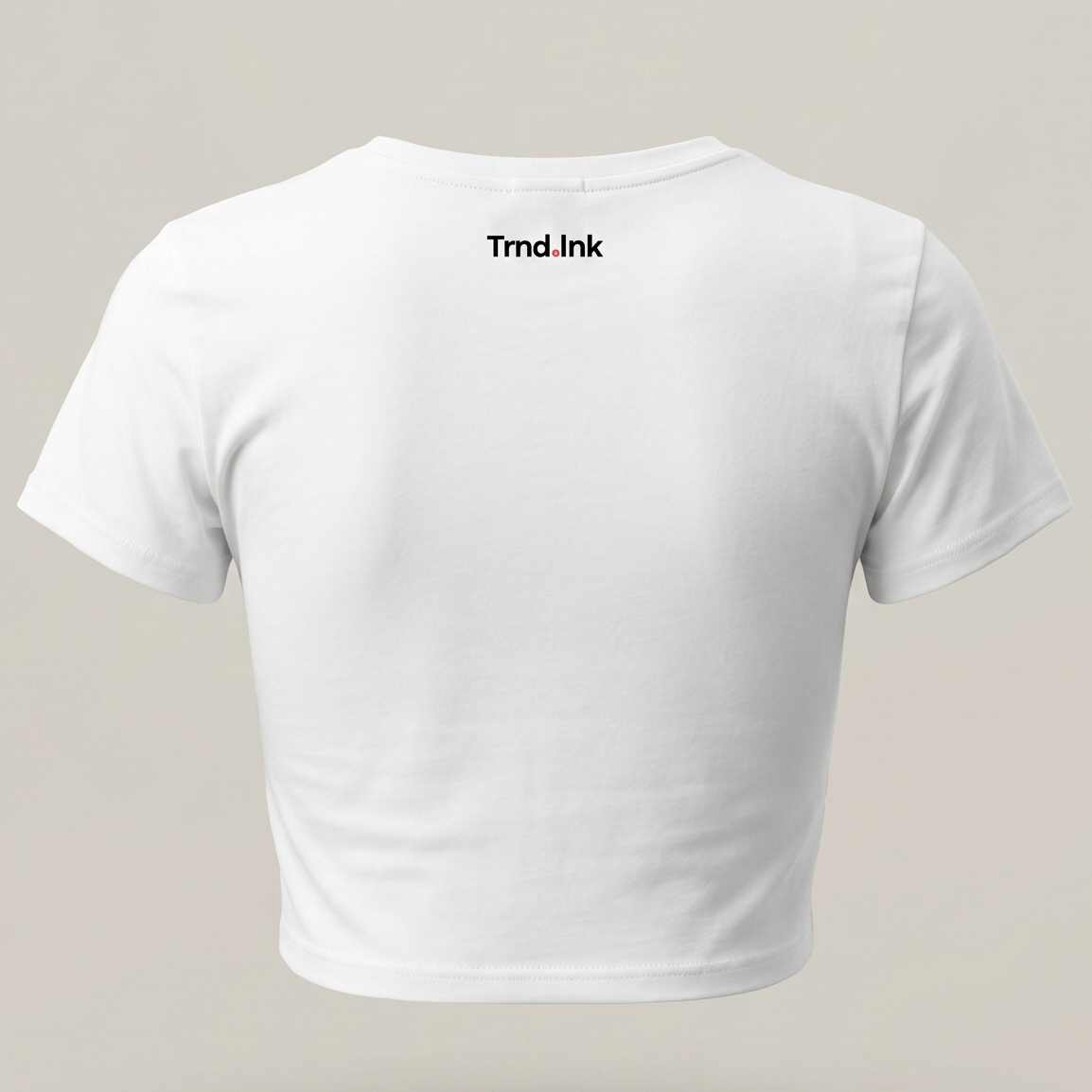 Una imagen de la parte trasera de una camiseta corta blanca y ajustada de "Trnd.Ink". La camiseta tiene cuello redondo y mangas cortas. El logotipo de "Trnd.Ink" está impreso en la parte superior central de la espalda, en un pequeño rectángulo blanco con texto negro y un pequeño círculo rojo al final. El fondo es de color gris claro.