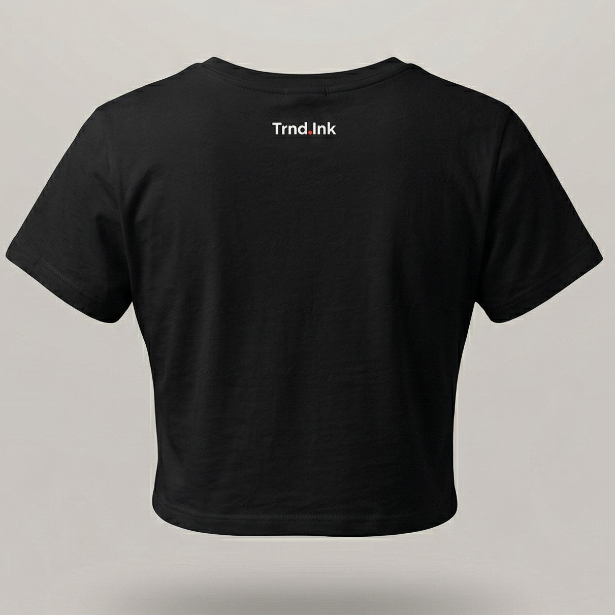 Parte trasera de un crop top negro para mujer de trnd.ink, mostrando el logo pequeño de la marca en blanco centrado en la parte superior de la espalda, diseño minimalista urbano.