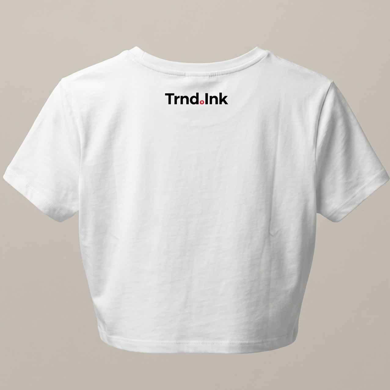 Mockup de camiseta blanca tipo crop top para mujer, mostrando el logo de Trnd.ink estampado en negro y rojo en la parte superior central de la espalda sobre un fondo neutro.