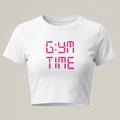 Camiseta crop top blanca de manga corta con un diseño gráfico central que dice "GYM TIME" en un estilo de fuente LED digital de color rosa fucsia.