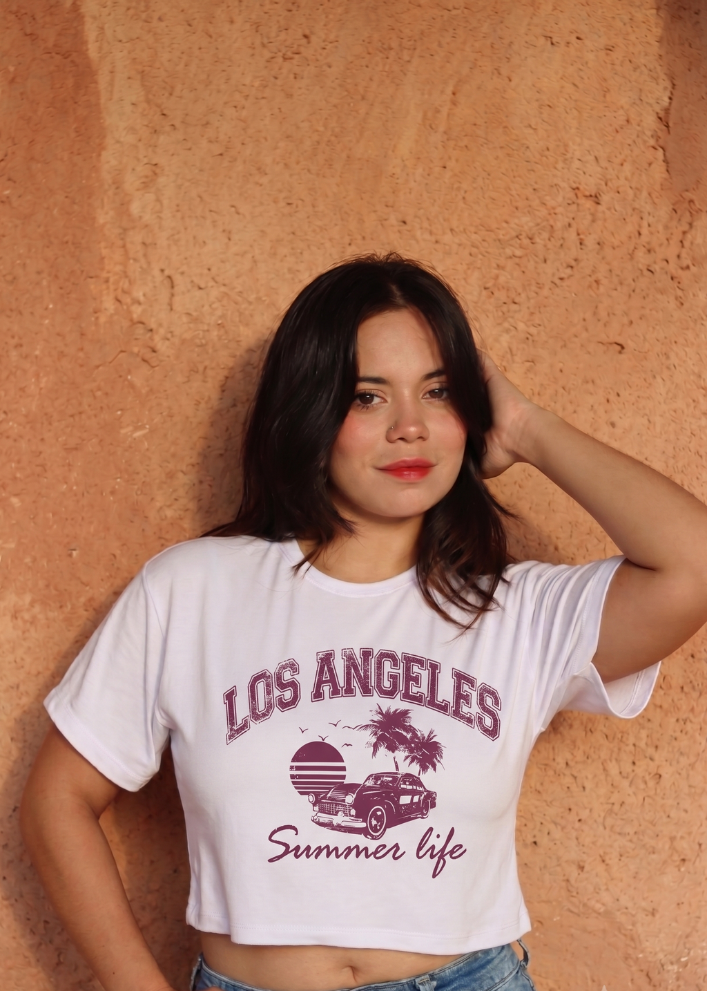 Crop top blanco para mujer con estampado urbano de Los Angeles Summer Life, combinado con jean de tiro alto ante fondo texturizado.