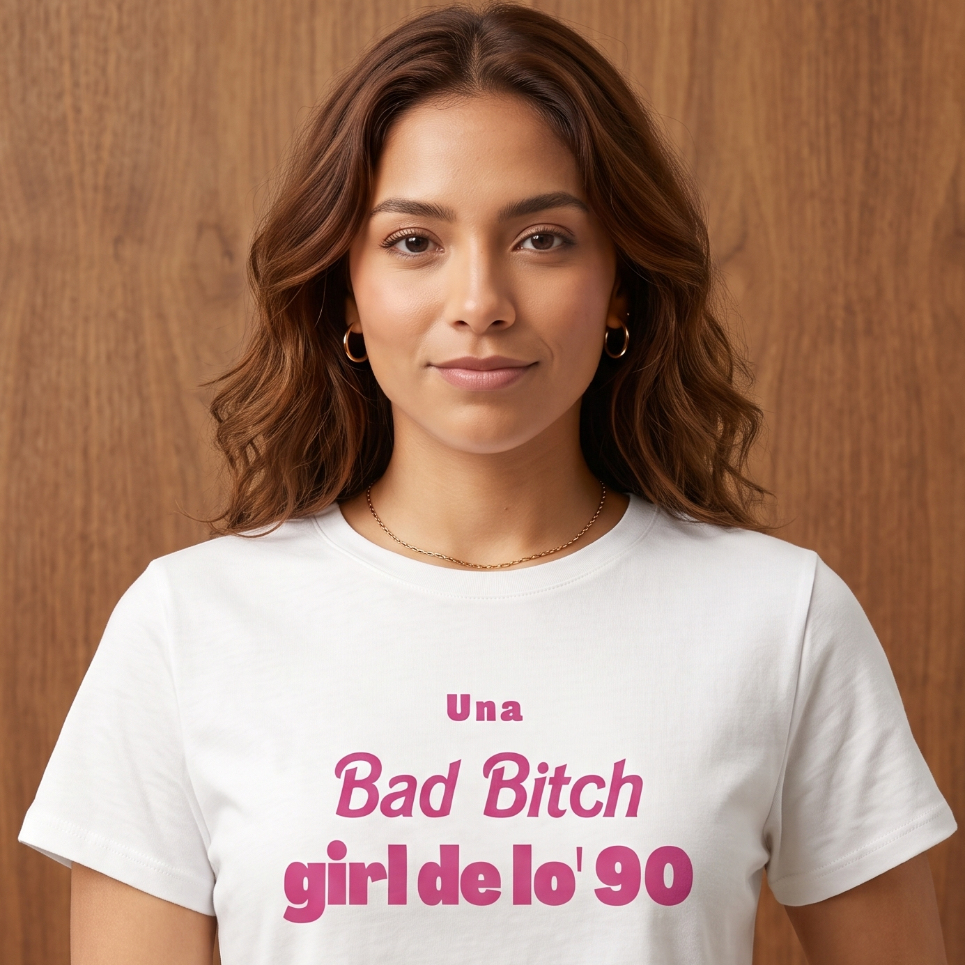 Camiseta blanca tipo crop top para mujer con la frase "Una Bad Bitch girl de lo' 90" estampada en letras color rosa. Modelo vistiendo la prenda con jeans de tiro alto sobre un fondo de madera.