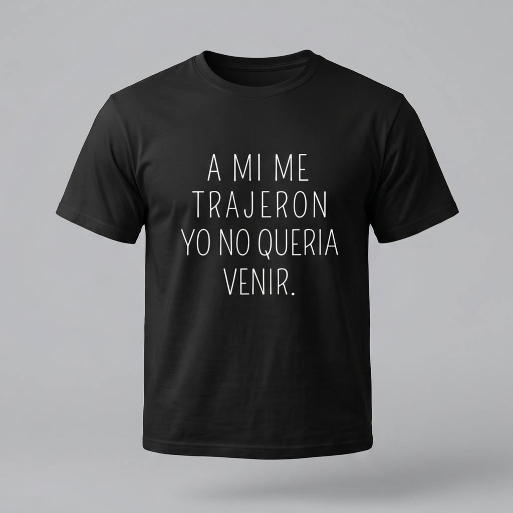 Una camiseta de algodón negra de manga corta con la frase en español 'A MI ME TRAJERON YO NO QUERIA VENIR.' impresa en la parte delantera en letras blancas finas y centradas. El fondo es de color gris claro.