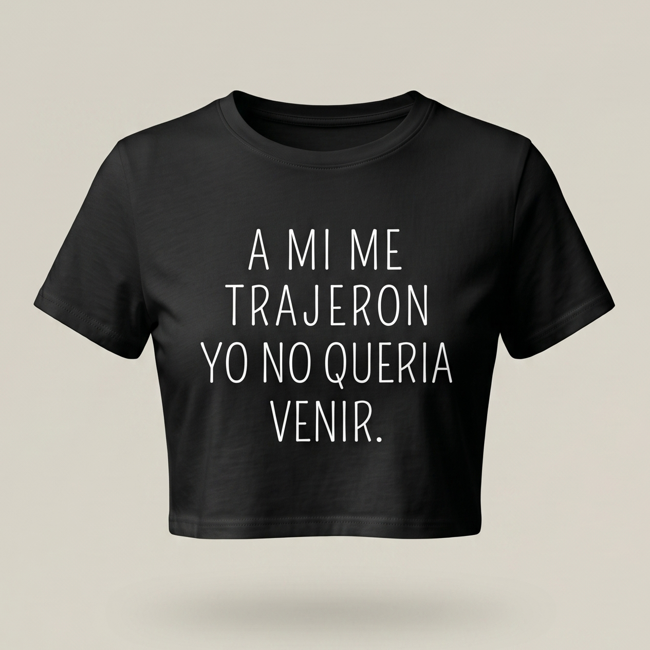 Camisa tipo crop top de color negro para mujer con la frase 'A MI ME TRAJERON YO NO QUERIA VENIR' estampada en letras blancas minimalistas sobre fondo neutro.